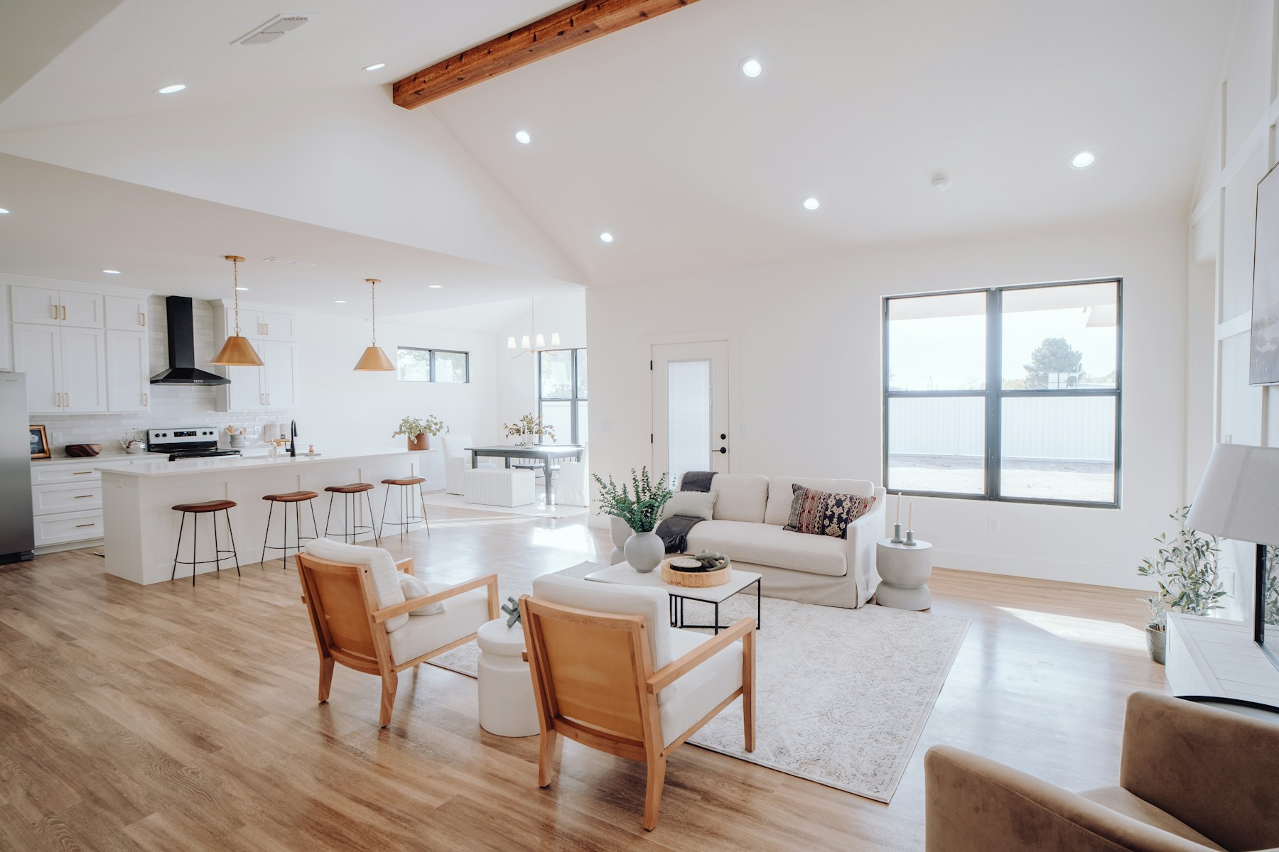 A bright living room with a white sofa, wood flooring, and an open kitchen.